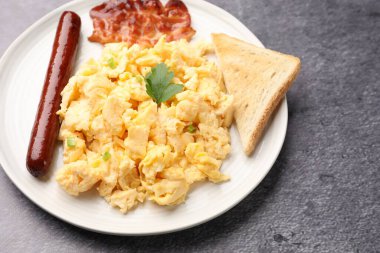 Lezzetli bir kahvaltı. Yağda yumurta, domuz pastırması, sosis ve ekmek. Gri desenli masada servis ediliyor. Yakın plan.