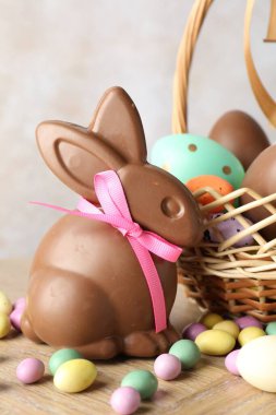 Çikolatalı Paskalya tavşanı ve hasır sepetteki yumurtalar ahşap masada açık gri arka planda, yakın plan