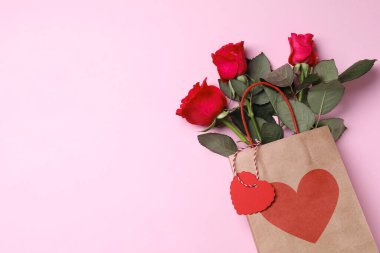 Pembe arka planda güller olan kağıt torba, üst manzara. Metin için boşluk