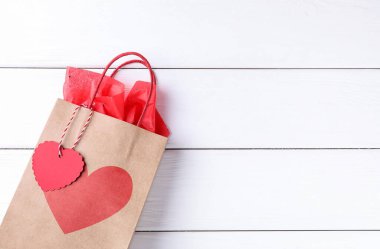 Beyaz ahşap arka planda kalbi olan hediye çantası, üst görünüm ve metin için yer. Sevgililer Günü