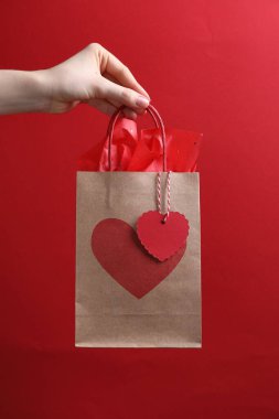 Kırmızı arka planda kalbi olan hediye paketi tutan kadın, yakın plan. Sevgililer Günü