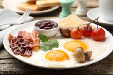 Geleneksel İngiliz kahvaltısı. Lezzetli, güneşli tarafı domuz pastırmalı, kırmızı fasulyeli, domatesli, mantarlı ve ahşap masada servis edilen kızarmış ekmekli yumurtalar.