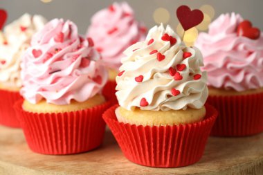 Sevgililer Günün kutlu olsun. Tahta zemin üzerinde kalp şeklinde tepeleri olan lezzetli kapkekler gri arka planda, bulanık ışıkları olan, yakın plan...