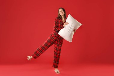 Kırmızı arka planda yastıklı şık pijamalı mutlu kadın.