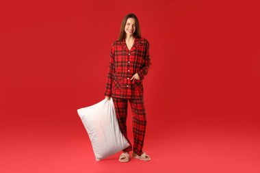 Kırmızı arka planda yastıklı şık pijamalı mutlu kadın.