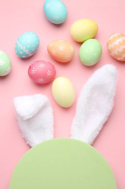 Mutlu Paskalyalar. Şirin tavşan kulakları, boyalı yumurtalar ve pembe arka planda boş podyum, düz uzanma.