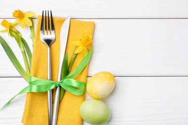 Paskalya sofrası. Nergisli güzel gümüş takımlar ve beyaz ahşap arka planda boyanmış yumurtalar, üst manzara. Metin için boşluk