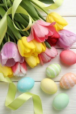 Boyalı Paskalya yumurtaları, güzel laleler ve beyaz ahşap masa üzerinde kurdele, düz uzanmış.