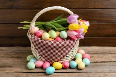 Hasır sepete boyanmış Paskalya yumurtaları ve ahşap masada güzel laleler.