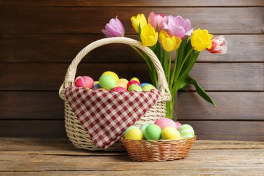Hasır sepete boyanmış Paskalya yumurtaları ve ahşap masada güzel laleler.