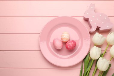 Paskalya kutlaması. Çiçeklerle süslü bir ortam ve pembe ahşap masaya boyanmış yumurtalar. Metin için boşluk