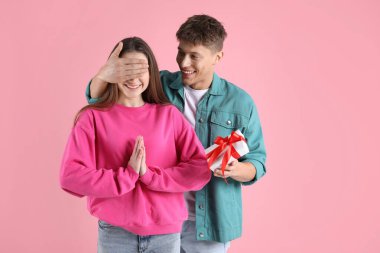 Sevgililer Günü. Mutlu genç adam pembe arka planda kız arkadaşına sürpriz yapıyor.