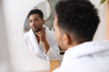 Yakışıklı adam aynada kendine bakıyor.