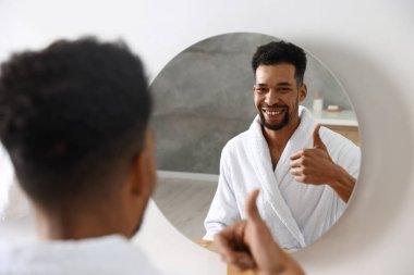 Mutlu adam aynada yansımasına başparmak işareti yapıyor.