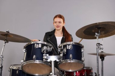 Açık gri arka planda bagetleri ve davulları olan genç bir kız.