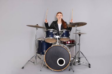 Açık gri arka planda bagetleri ve davulları olan genç bir kız.