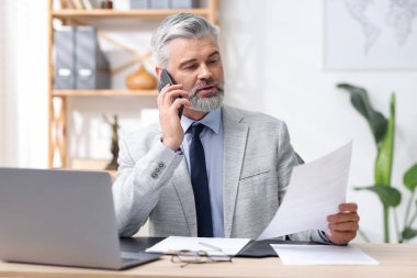 Ofiste akıllı telefonla konuşan takım elbiseli yakışıklı bir işadamı.