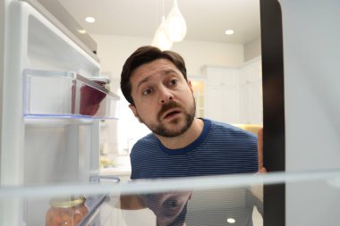 Adam mutfaktaki açık buzdolabına bakıyor, içeriden bakıyor.