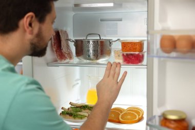 Mutfakta açık buzdolabına bakan bir adam var.