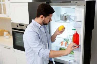 Mutfakta limonlu bir adam açık buzdolabının yanında.