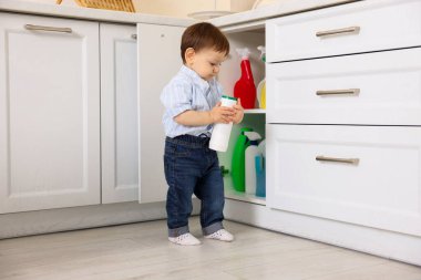 Evde çocuk güvenliği. Küçük çocuk mutfakta temizlik ürünleriyle dolap açıyor.