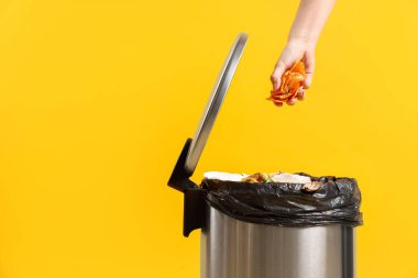 Mandalina kabuklarını sarı arka plandaki çöp kutusuna atan kadın, yakın plan. Metin için boşluk