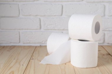 Beyaz tuğla duvarın yanındaki ahşap masada tuvalet kağıdı ruloları, yakın plan. Metin için boşluk