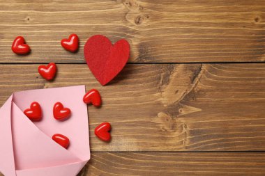Sevgi. Ahşap masada üzerinde kırmızı dekoratif kalpler olan pembe bir zarf. Metin için boşluk
