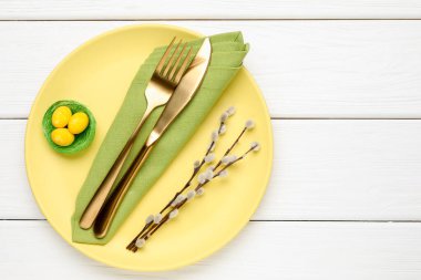 Paskalya kutlaması. Çatal bıçak takımı, söğüt dalları ve beyaz ahşap masaya boyanmış yumurtalar, üst manzara. Metin için boşluk