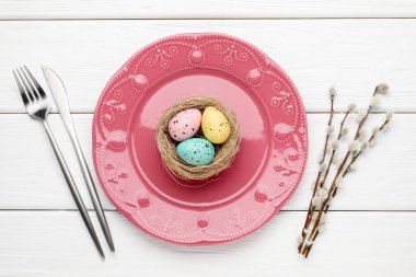 Paskalya kutlaması. Çatal bıçak takımları, söğüt dalları ve beyaz ahşap masaya boyanmış yumurtalar.