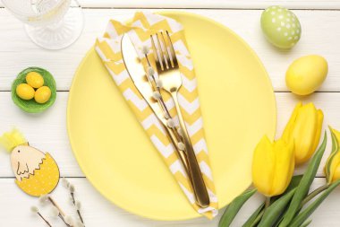 Paskalya kutlaması. Çatal bıçak takımları, söğüt dalları, çiçekler ve beyaz ahşap masaya boyanmış yumurtalar.