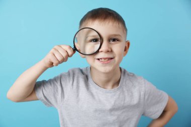 Açık mavi arka planda büyüteç takan küçük çocuk.