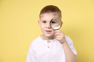 Sarı arka planda büyüteç olan küçük çocuk.