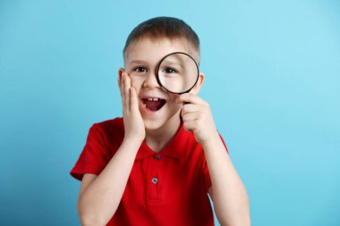 Açık mavi arka planda büyüteç olan küçük çocuk şaşırdı.