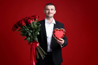 Sevgililer Günü kutlaması. Güzel gül buketi ve kırmızı arka planda mumları olan bir adam.