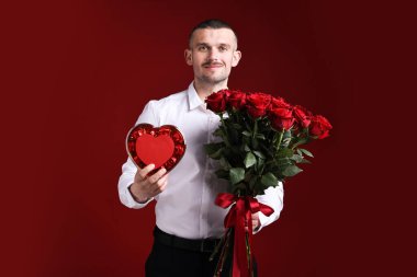 Sevgililer Günü kutlaması. Kırmızı arka planda gül buketi ve şekerlemeleri olan bir adam.
