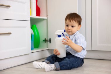 Evde çocuk güvenliği. Küçük çocuk mutfakta temizlik ürünleriyle dolap açıyor.