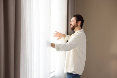 Evde şık pencere perdeleri açan adam