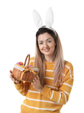 Paskalya kutlaması. Saç bandı takmış, tavşan kulaklı, hasırdan sepet dolusu beyaz arka planda boyalı yumurtaları olan gülümseyen bir kadın.