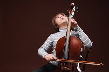 Kahverengi arka planda keman çalan sevimli küçük çocuk, metin için yer var.