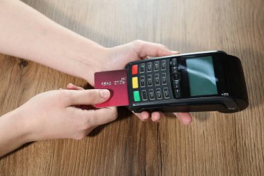 Kredi kartı olan bir kadın ahşap masada ödeme terminalini kullanıyor.