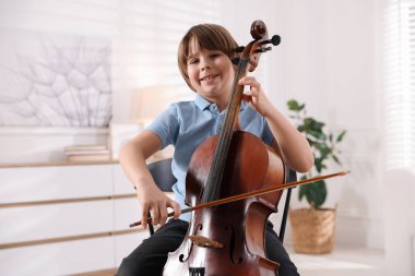 Evdeki sandalyede keman çalan küçük çocuk.