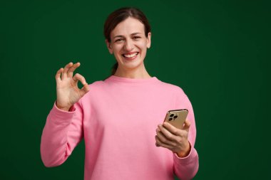 Akıllı telefonlu mutlu kadın yeşil arka planda iyi bir hareket gösteriyor.