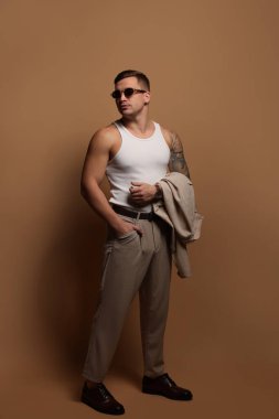 Moda modeli. Güneş gözlüklü yakışıklı adam bej arka planda poz veriyor.