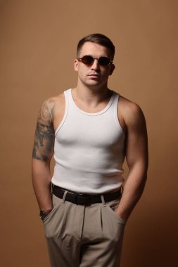 Moda modeli. Güneş gözlüklü yakışıklı adam bej arka planda poz veriyor.