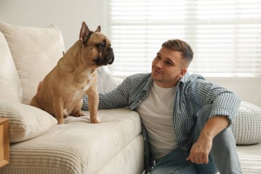 Evdeki kanepenin yanında tatlı köpeğiyle rahatlayan genç bir adam.