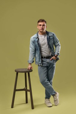 Moda modeli. Yeşil arka planda dışkısı olan gözlüklü ve ceketli yakışıklı bir adam.