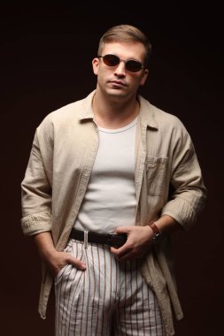 Moda modeli. Siyah arka planda poz veren güneş gözlüklü yakışıklı bir adam.