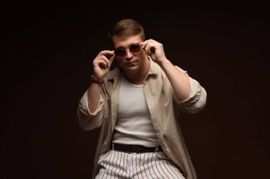 Moda modeli. Siyah arka planda poz veren güneş gözlüklü yakışıklı bir adam.