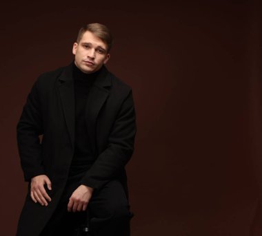 Moda modeli. Koyu kahverengi arka planda poz veren yakışıklı adamın portresi, metin için boşluk